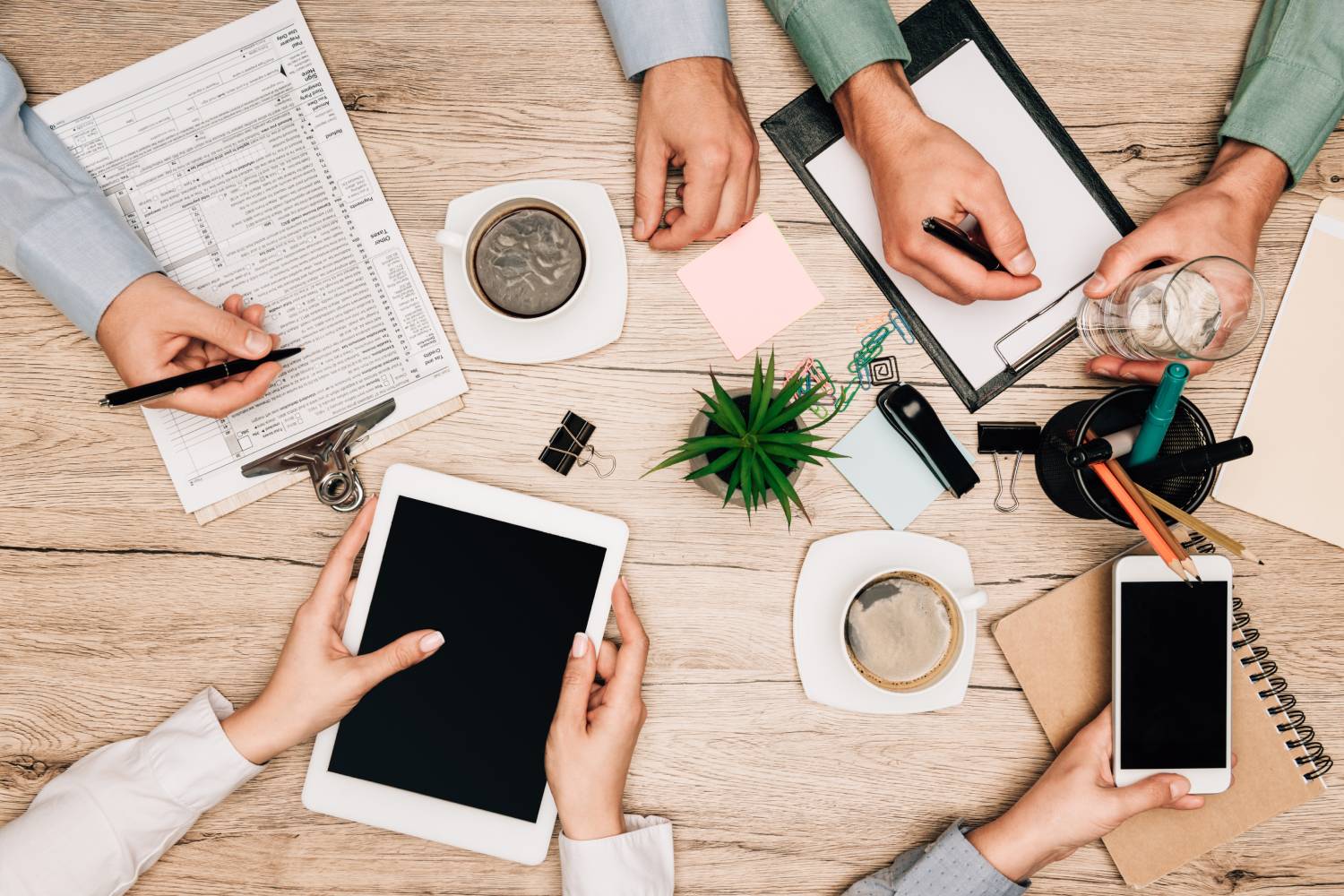Top view of colleagues working with gadgets and documents with coffee on table, cropped view